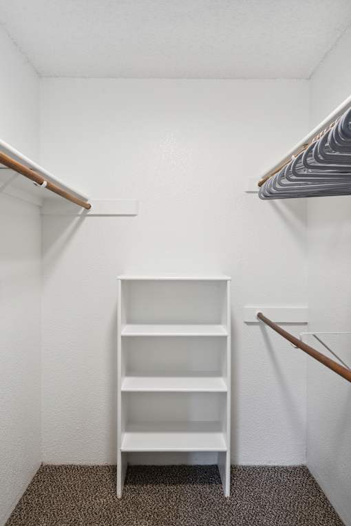 A white shelf unit with three shelves is in a white room.