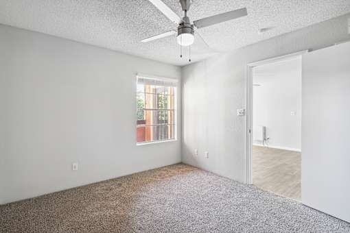 A room with a ceiling fan and a window overlooking a balcony.