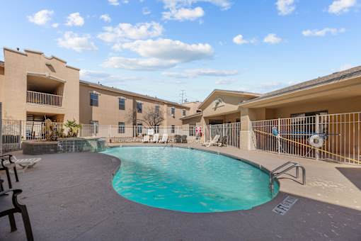 A swimming pool in front of a building with a blue sky and clouds in the background.