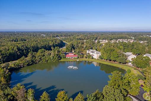 A serene lake surrounded by lush greenery and a few buildings in the distance.