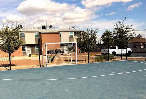 A basketball court is surrounded by a fence and a building.
