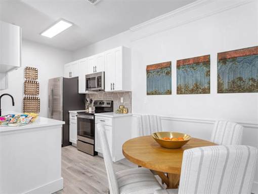 A kitchen with a table and chairs in the foreground and a painting on the wall.