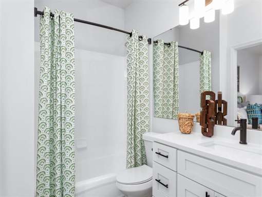 A bathroom with a toilet, sink, and green patterned shower curtains.