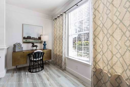 A room with a desk and chair in front of a window with blinds.