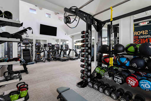 A gym with a variety of equipment including dumbbells, weight plates, and a bench.