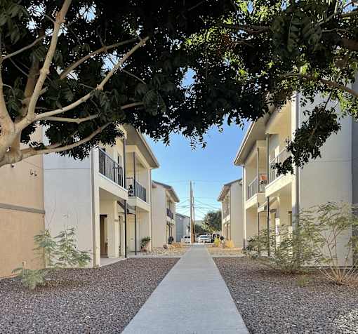 A tree-lined walkway leads between two rows of modern townhouses.