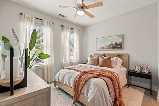 A bedroom with a bed, a ceiling fan, and a painting on the wall.