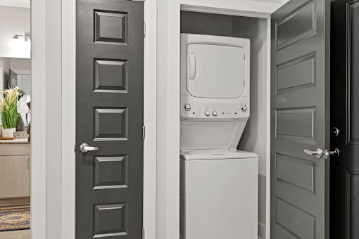 A white washing machine is in a doorway between two rooms.