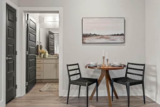 A dining room with a table set for two and a painting on the wall.