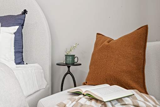 A cozy bedroom scene with a book, a cup, and a pillow.