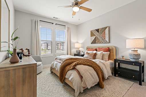 A bedroom with a bed, a chair, a table, and a ceiling fan.