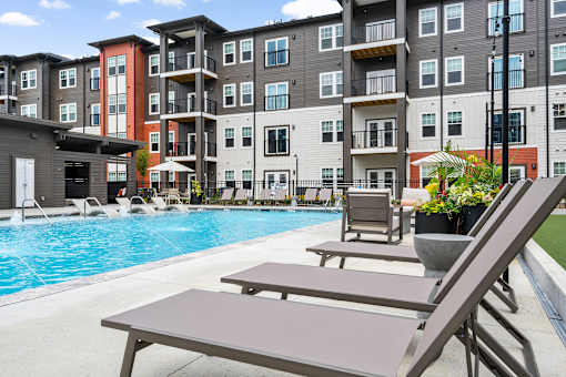 A pool area with lounge chairs and a table in front of apartment buildings.