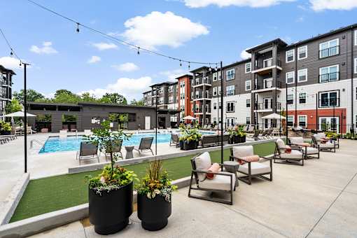 A pool area with chairs and plants in front of apartment buildings.