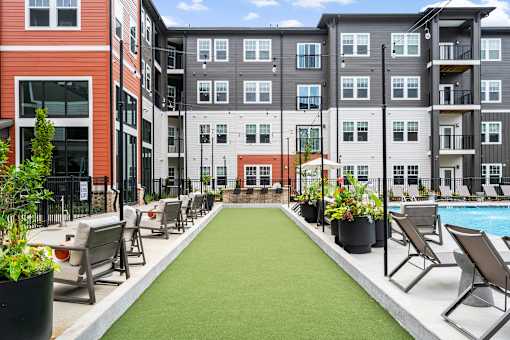 A pool surrounded by chairs and plants in front of apartment buildings.