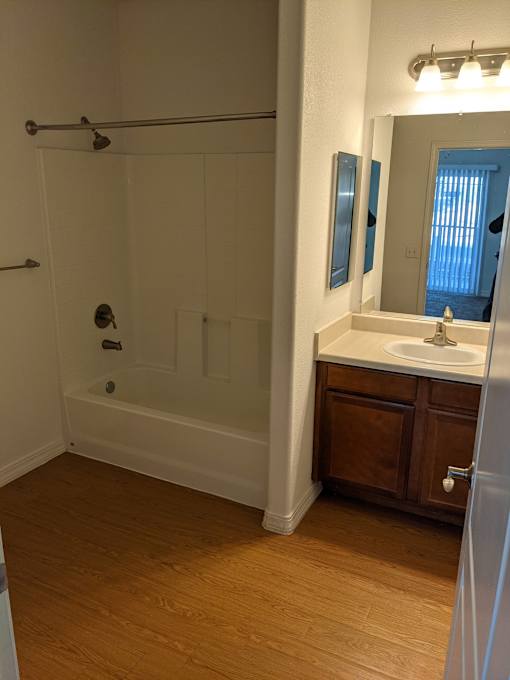 A bathroom with a white tub, wooden floors, and a white sink.