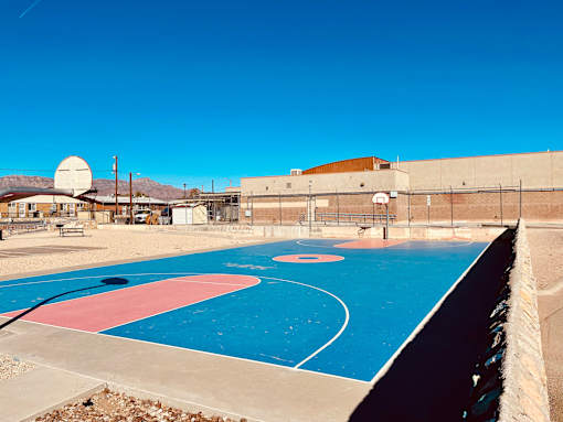 A basketball court with a blue and pink surface and a basketball hoop.
