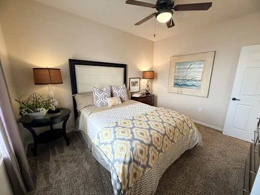 A bedroom with a bed, a ceiling fan, and a painting on the wall.