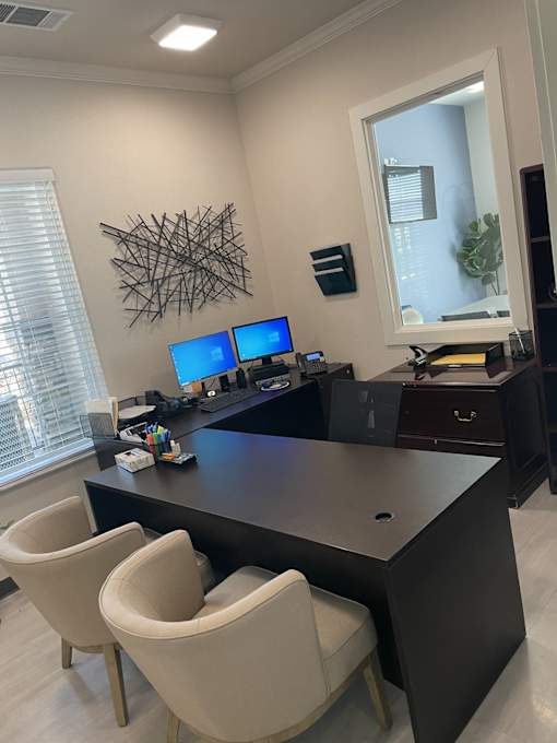A modern office with a large desk and two chairs.