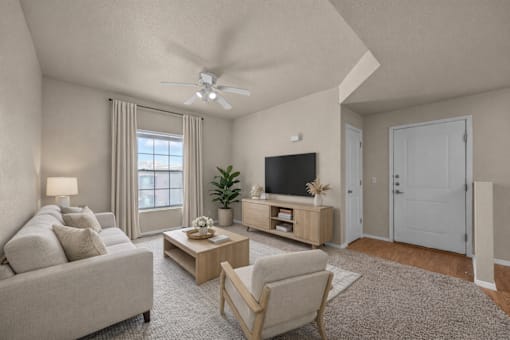 A living room with a grey couch, a wooden coffee table, a television, and a ceiling fan.