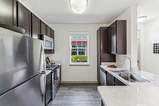 A kitchen with a stainless steel refrigerator and a window showing a building outside.