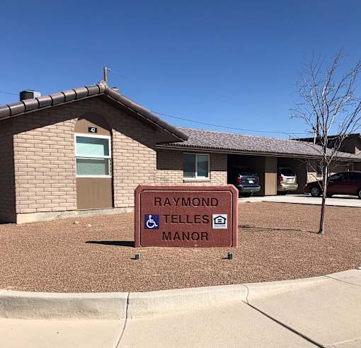 A sign in front of a building that says Raymond Telles Manor.