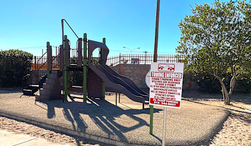 A sign in front of a playground warns that it is a towing enforced area.