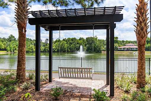 A wooden bench is under a pergola next to a lake.