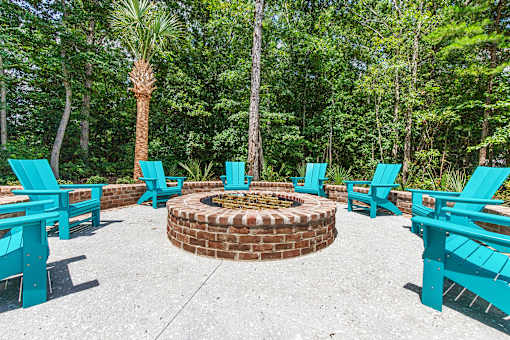 A fire pit surrounded by blue chairs in a forest setting.