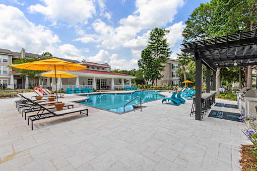 A pool with a yellow umbrella and blue chairs.