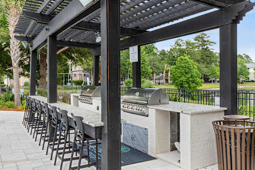 A barbecue grill is under a black pergola.