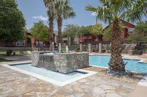 A pool with a waterfall and a palm tree in front of a red building.