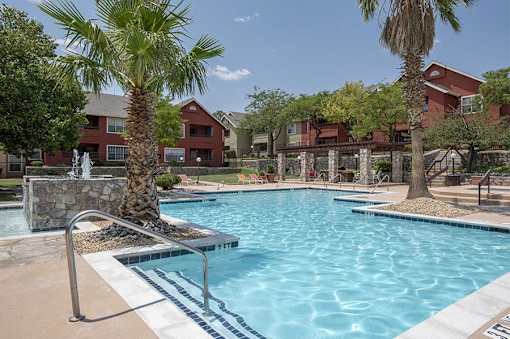 A pool surrounded by palm trees and a red building in the background.