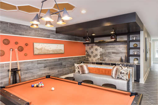 A pool table is in the middle of the club room with a couch and a shelf.