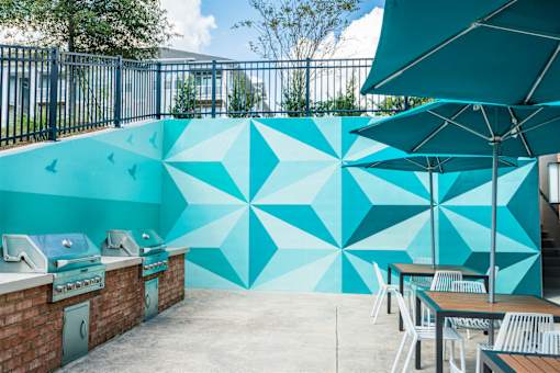 A wall with a geometric mural is behind a row of tables and grilling area.