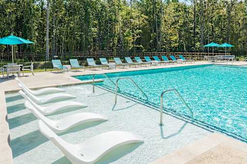 A pool with white lounge chairs and blue umbrellas.