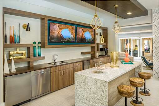 A modern kitchen in clubroom with stools and large televisions.