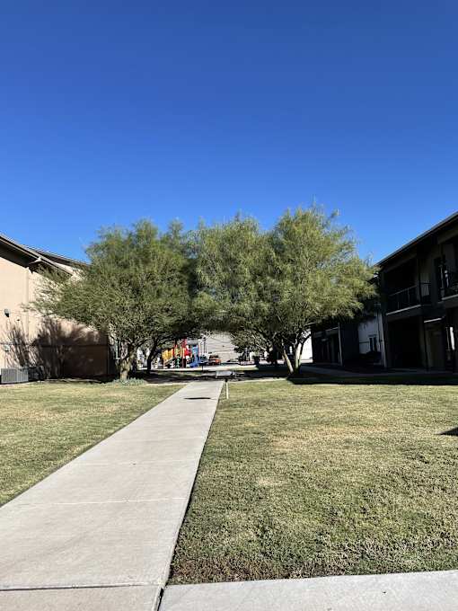A concrete walkway leads through a grassy area with trees on either side.