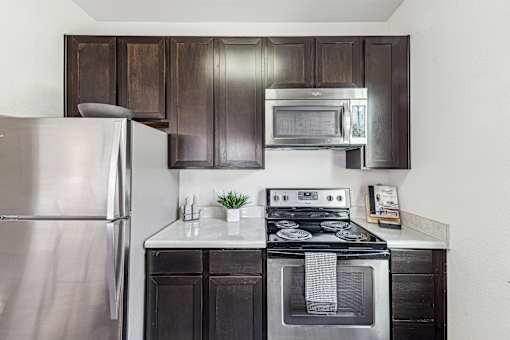 A modern kitchen with a stainless steel refrigerator, a stove with an oven, and dark brown cabinets.
