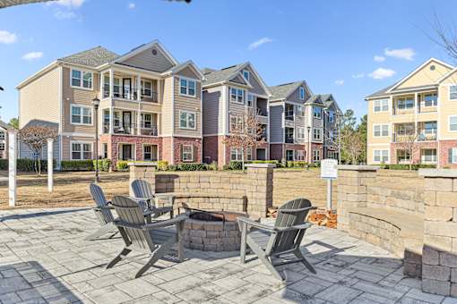 A patio with chairs and a fire pit in front of apartment buildings.