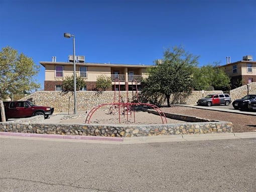 A playground with a red swing set is in front of a building.