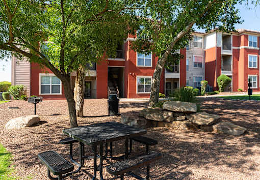 A black table and benches are set up in a courtyard with a red building in the background.