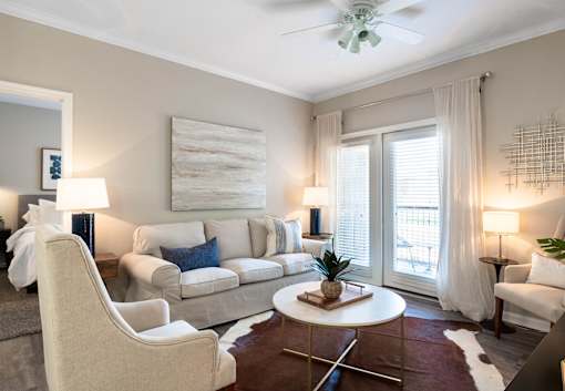 A living room with a white couch, a white chair, a white coffee table, a white rug, a white ceiling fan, a white wall, a white door, a white floor, a white table, a white lamp, a white