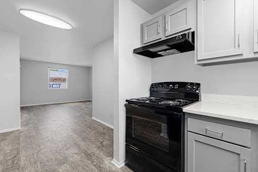 A black oven in a kitchen with white cabinets and a grey floor.