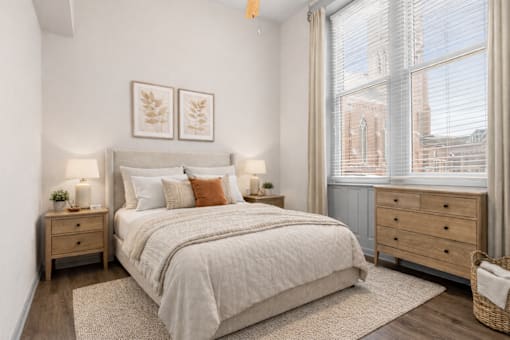 A bedroom with a large bed, two nightstands, and a window with a view of a cityscape.