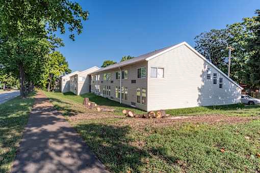 A white mobile home sits on a grassy lot with a sidewalk in front.
