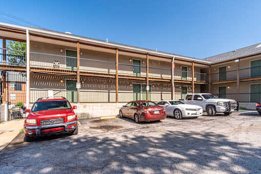 A red car is parked in a lot in front of a building.