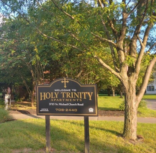 a sign for holy trinity apartments in front of a tree