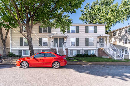 A red car is parked in front of a two-story house.