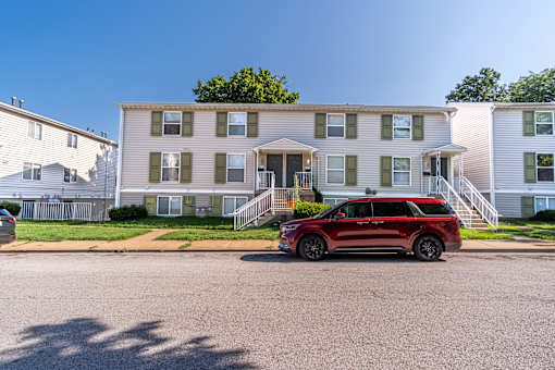 A red SUV is parked in front of a two-story apartment building.