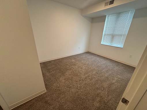A room with a carpeted floor and a window with blinds.